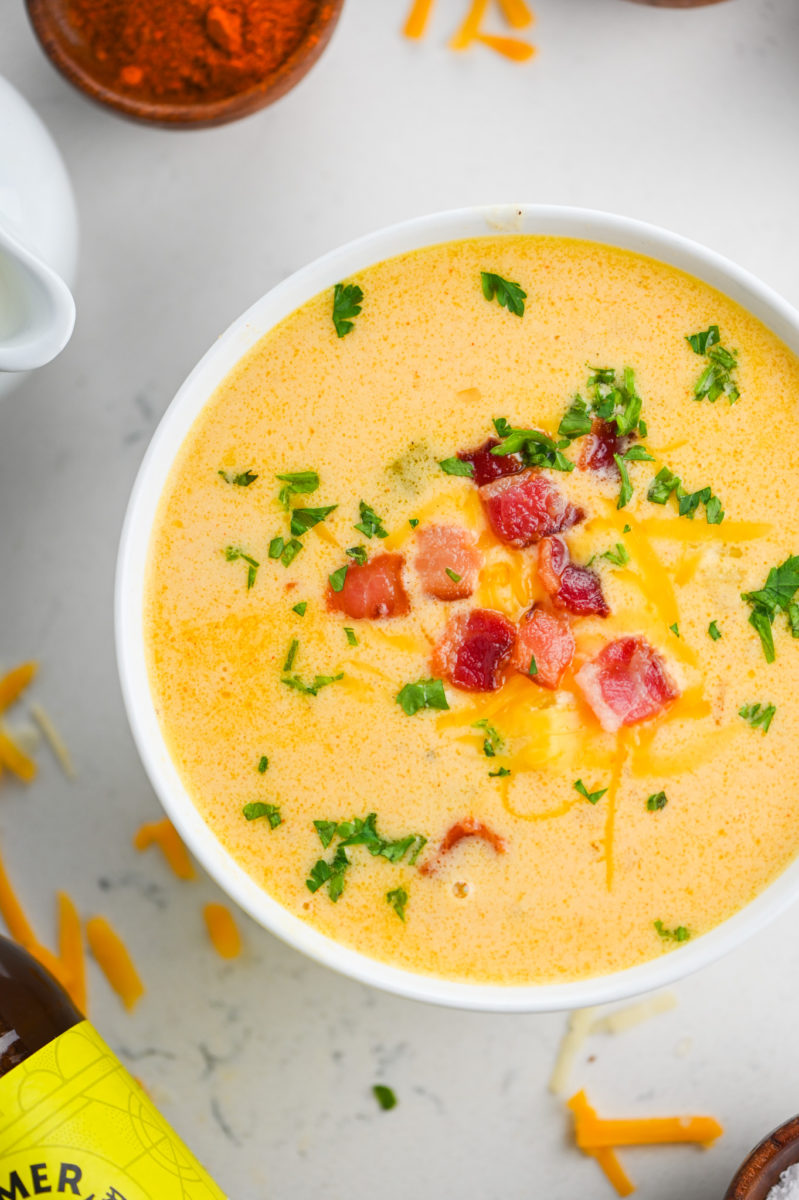 A bowl of beer cheese soup topped with bacon, cheddar cheese and parsley.