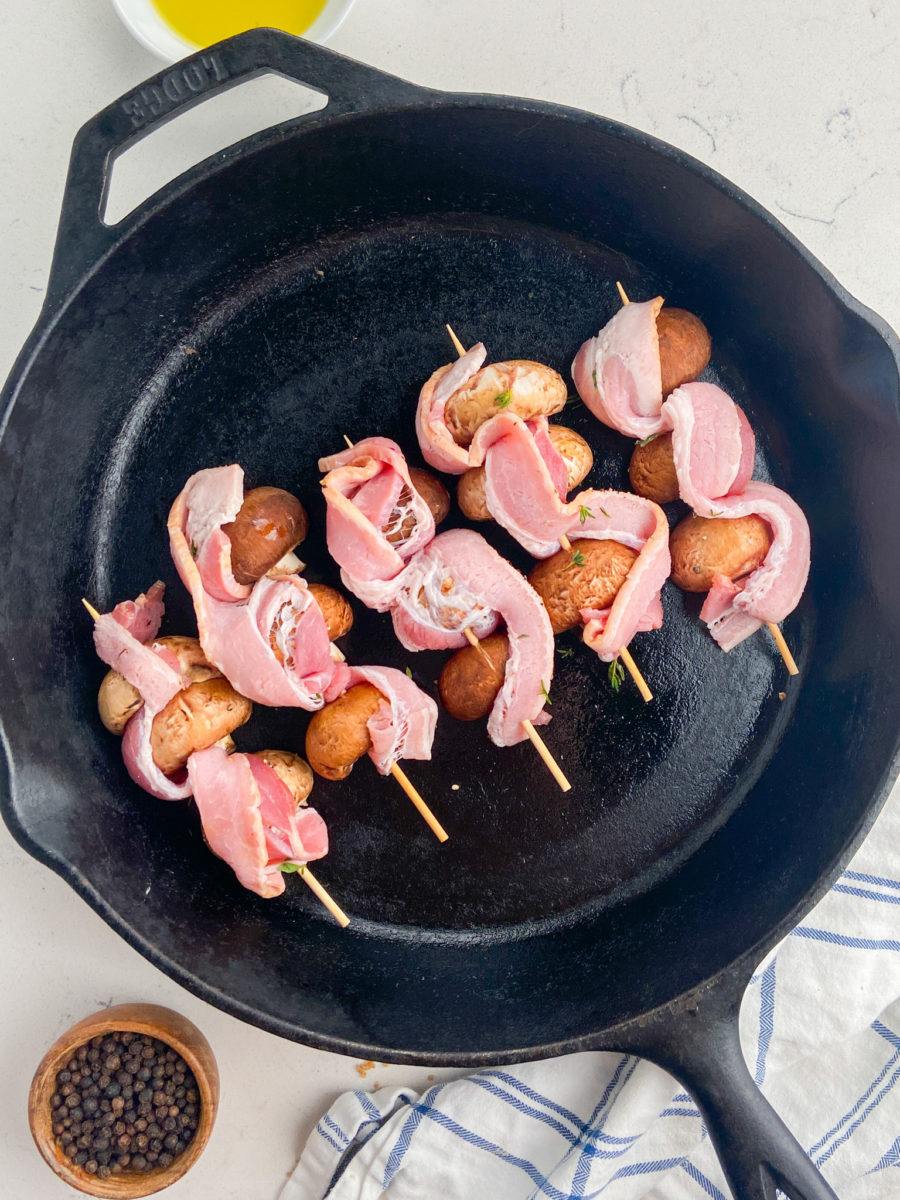 5 Mushroom bacon skewers in a cast iron skillet.
